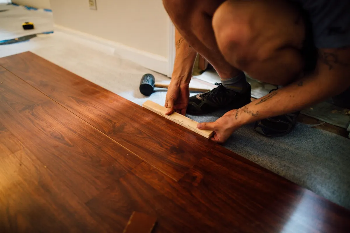 Worker installing laminate flooring planks with a mallet